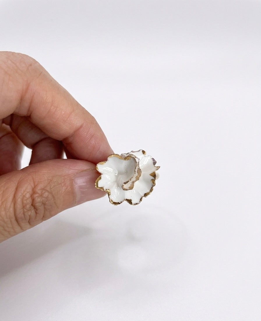 A hand holding a small white ceramic scalloped dish with gold edges