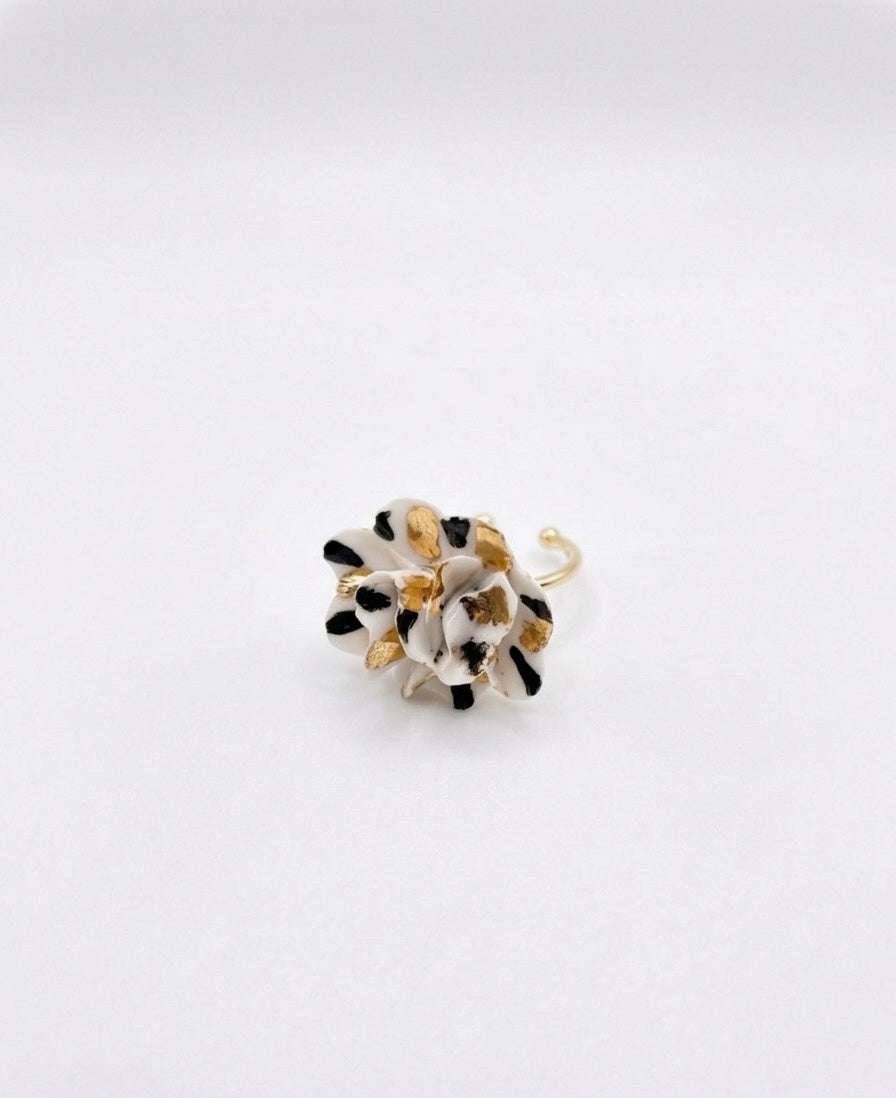 White and black speckled flower ring with gold details on a white background