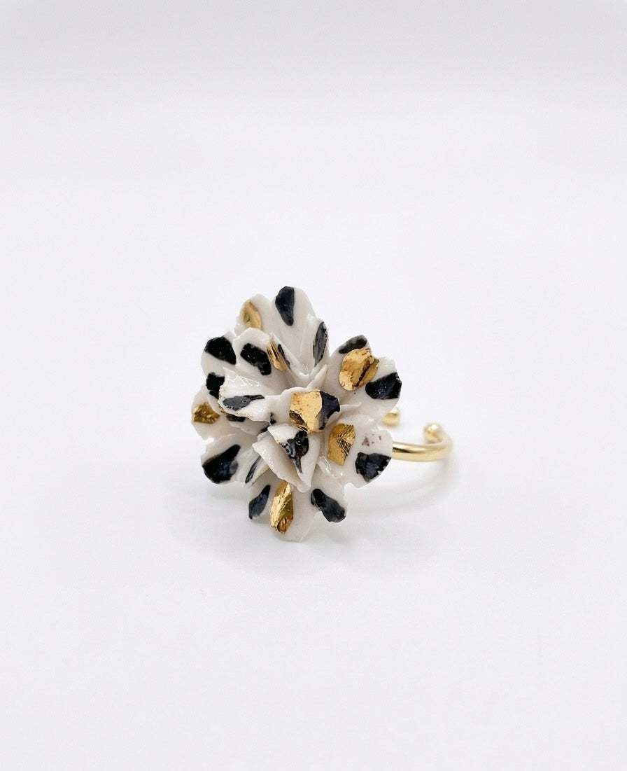 White ceramic flower ring with black spots and gold accents on a gold band