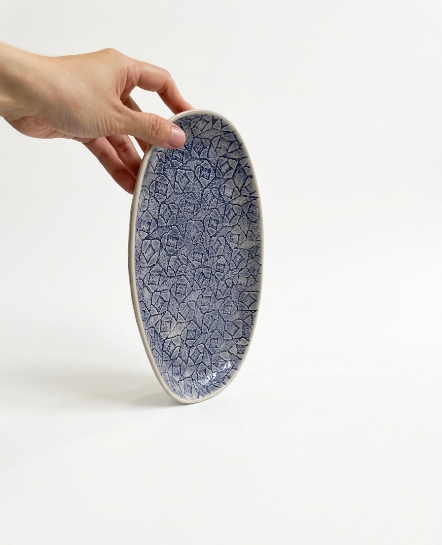 Đĩa gốm sứ oval vân đá xanh lam trên nền trắng, được cầm bằng tay