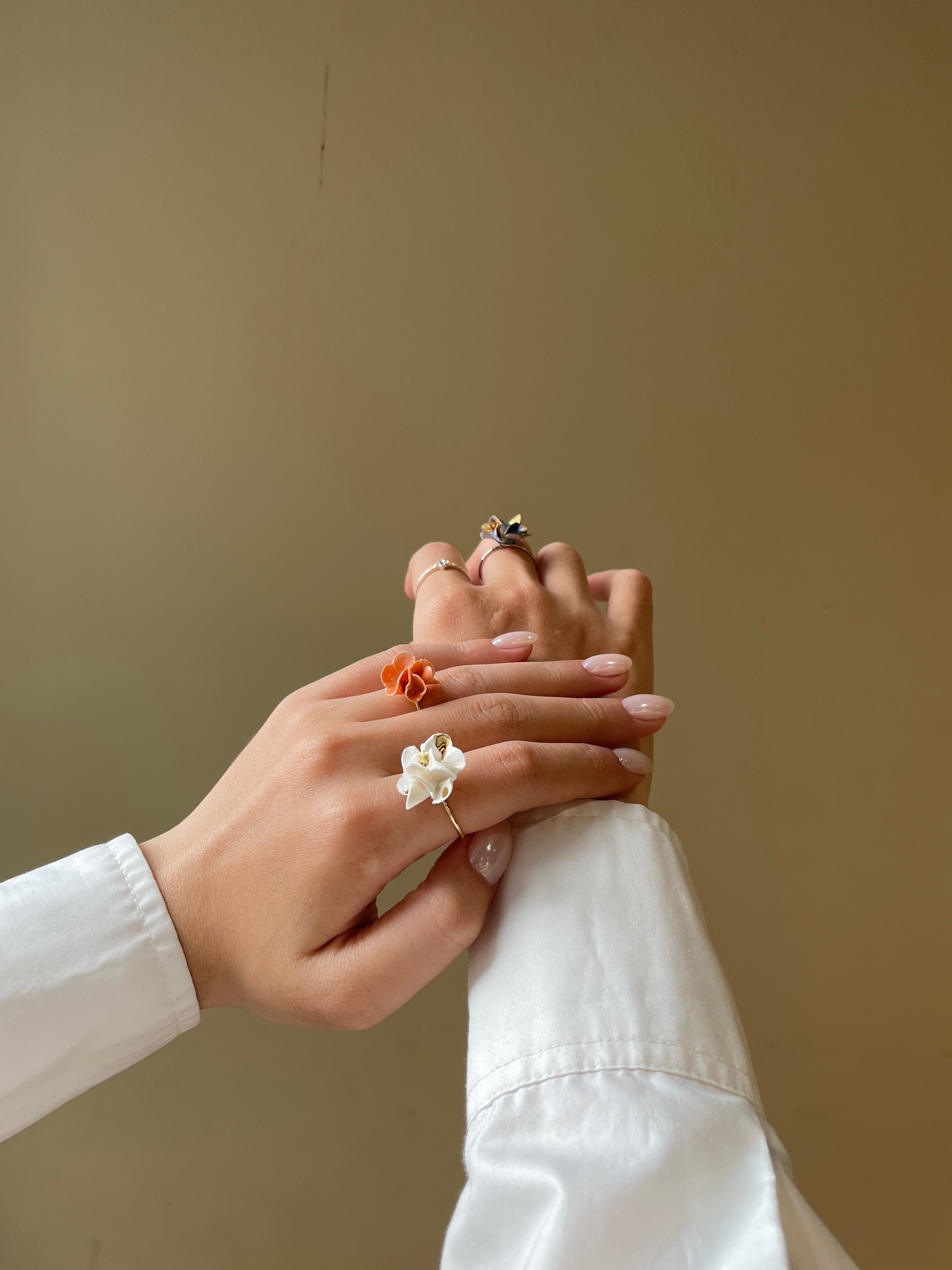 Hai bàn tay đeo nhẫn hoa trắng và cam nổi bật trên nền trung tính, phong cách nhẹ nhàng nữ tính